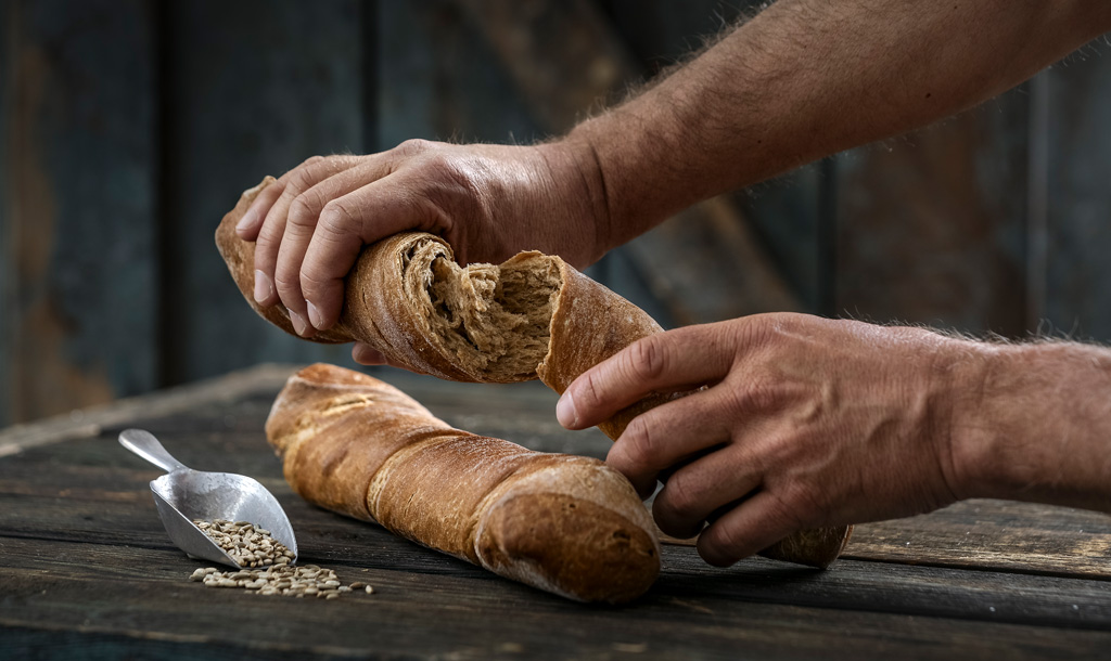 Bäckerhände brechen eine knusprige Brotstange - Bonnevit Feinbäckerei